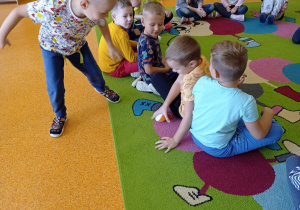 grupa grzecznie siedzi na dywanie jeden chłopiec maszeruje w koło nich
